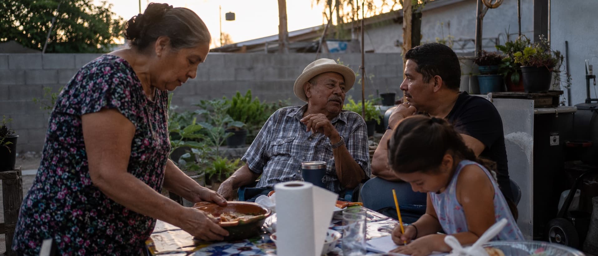 Three generations sharing dinner in the backyard at dusk.